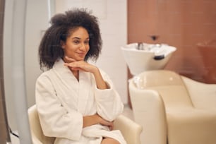 Charming Afro American woman keeping her hand under chin while glancing away with a smile