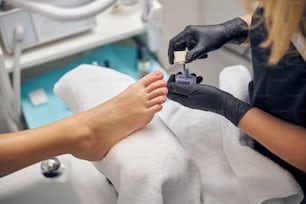 Top view close up of female foot while artist is holding bottle of cosmetic polish in beauty salon