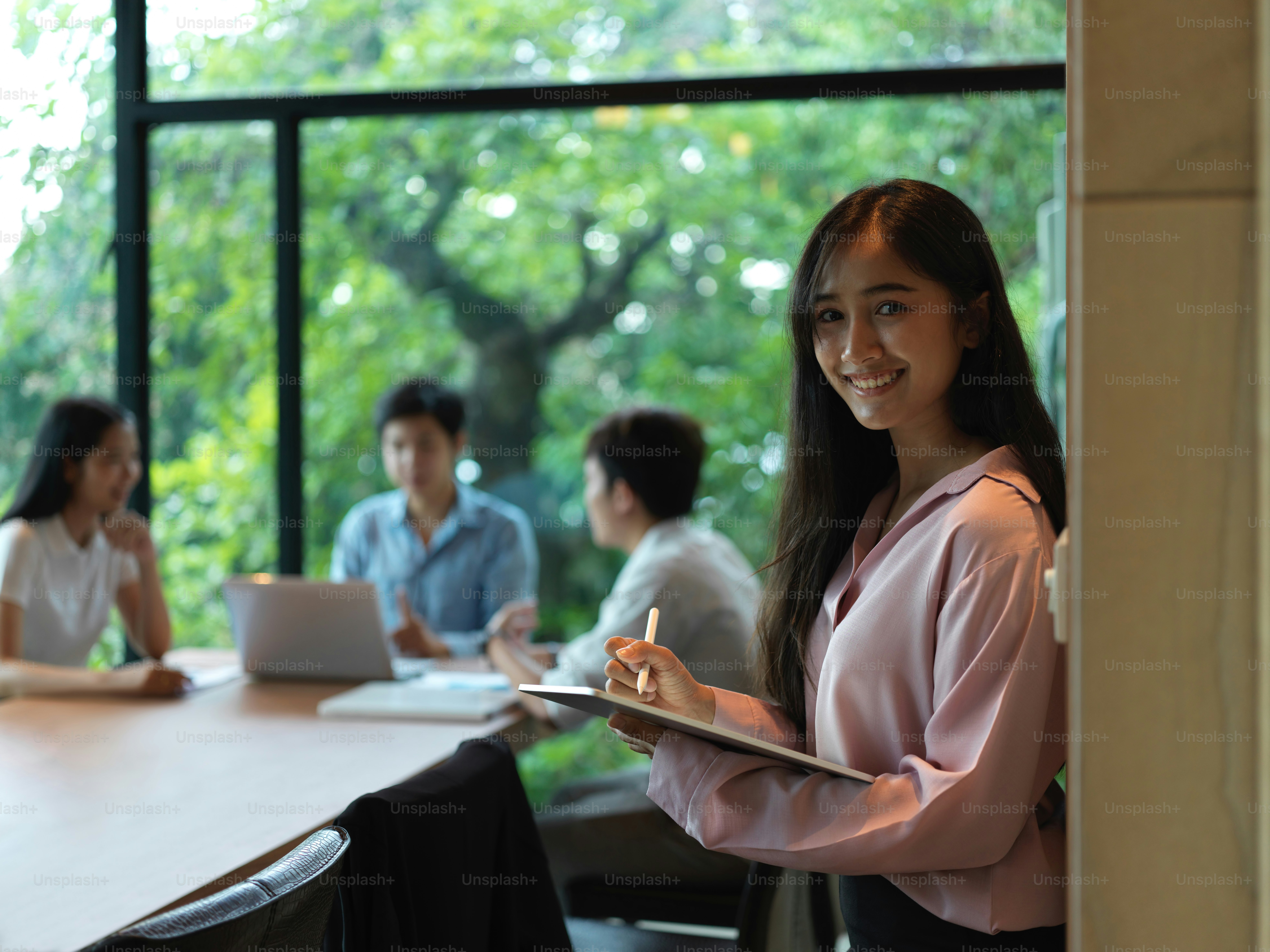 Portrait of female office worker smiling and using digital tablet while standing against wall in meeting room