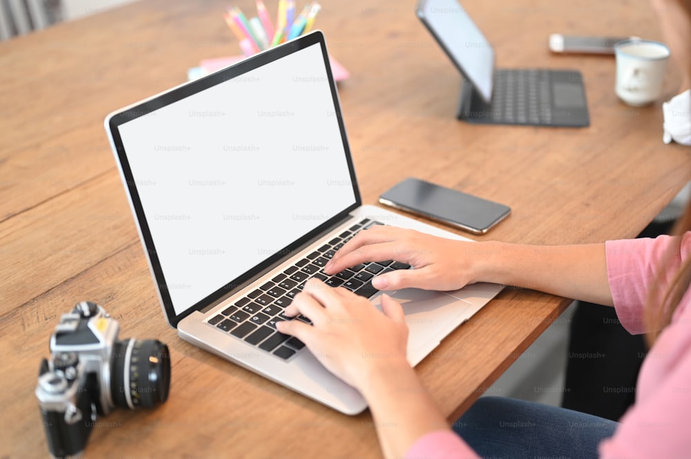 Uma imagem recortada de uma mulher está usando um laptop de tela branca em branco na mesa de madeira.