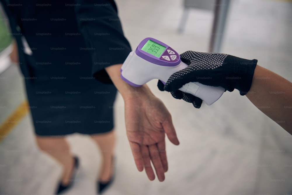 팬데믹 기간 동안 디지털 의료 온도계로 여성 체온을 측정하는 공항 경비원의 클로즈업