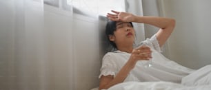 Une femme malade boit de l’eau et consomme une pilule alors qu’elle est allongée sur le lit de la chambre.