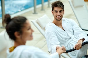 Junges, glückliches Paar in Bademänteln, das Händchen hält, während es im Wellnesscenter spricht. Der Mensch steht im Mittelpunkt.