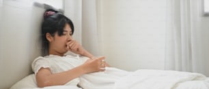 Une femme malade boit de l’eau et consomme une pilule alors qu’elle est allongée sur le lit de la chambre.