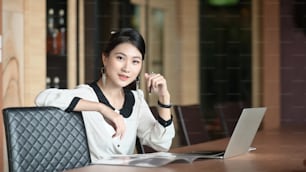 A young office woman is sitting with a computer laptop at the meeting table.