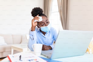 オフィスに一人で座り、風邪をひいて咳をしている女性。医療用マスクと手指消毒剤とストレスを抱えた女性。病気のオフィスで働くビジネスウーマンのショット。
