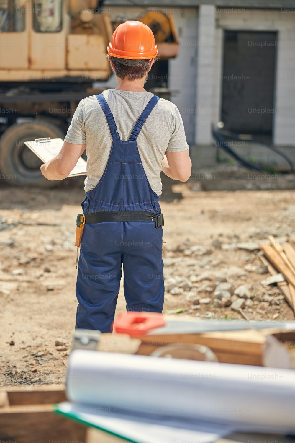 Back view of a worker with a clipboard in his hand standing at a construction site