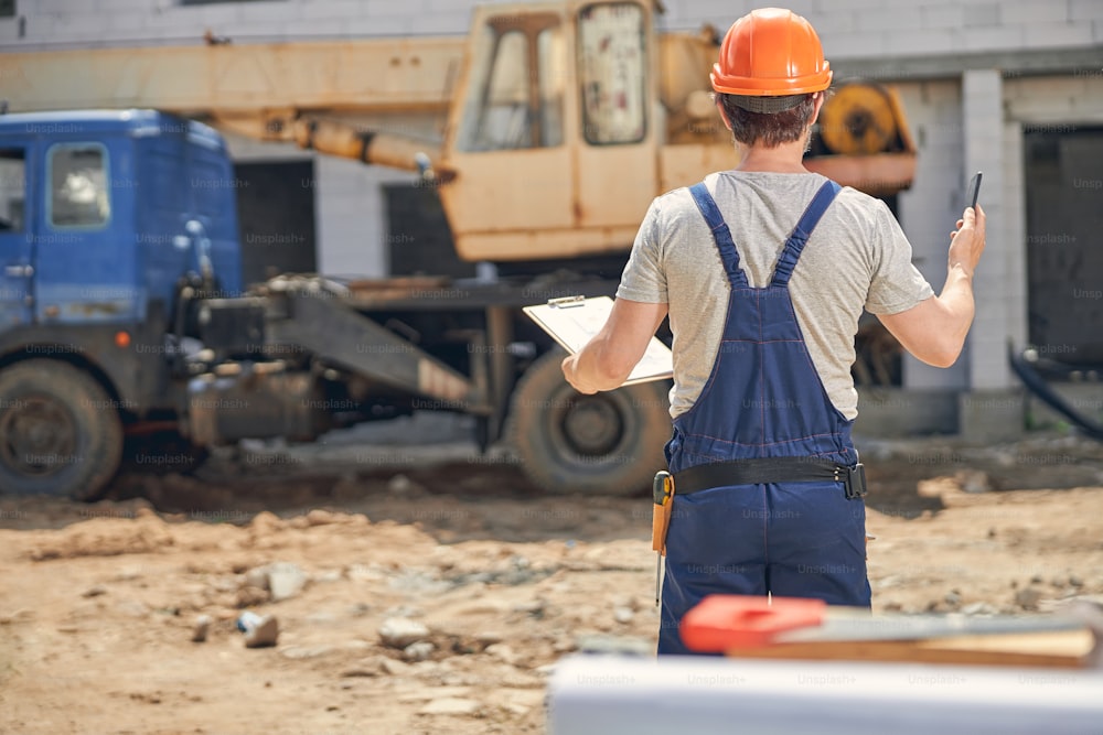 Back view of a man with a clipboard in his hand standing at a construction site