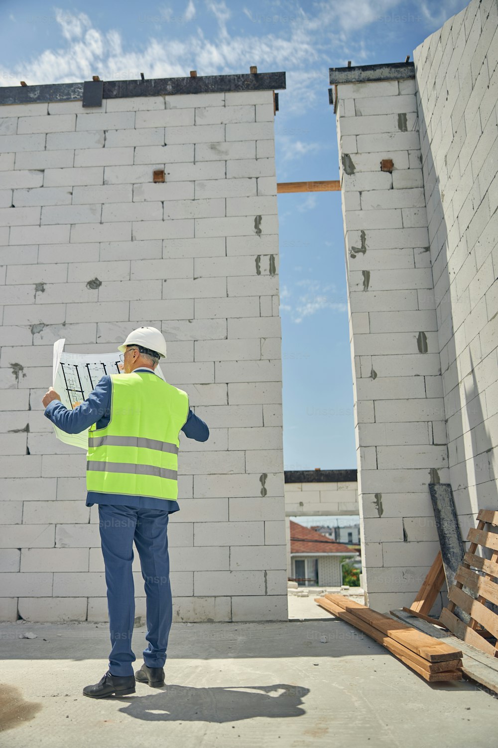 Back view of a grey-haired male worker standing in an unfinished house with bare walls