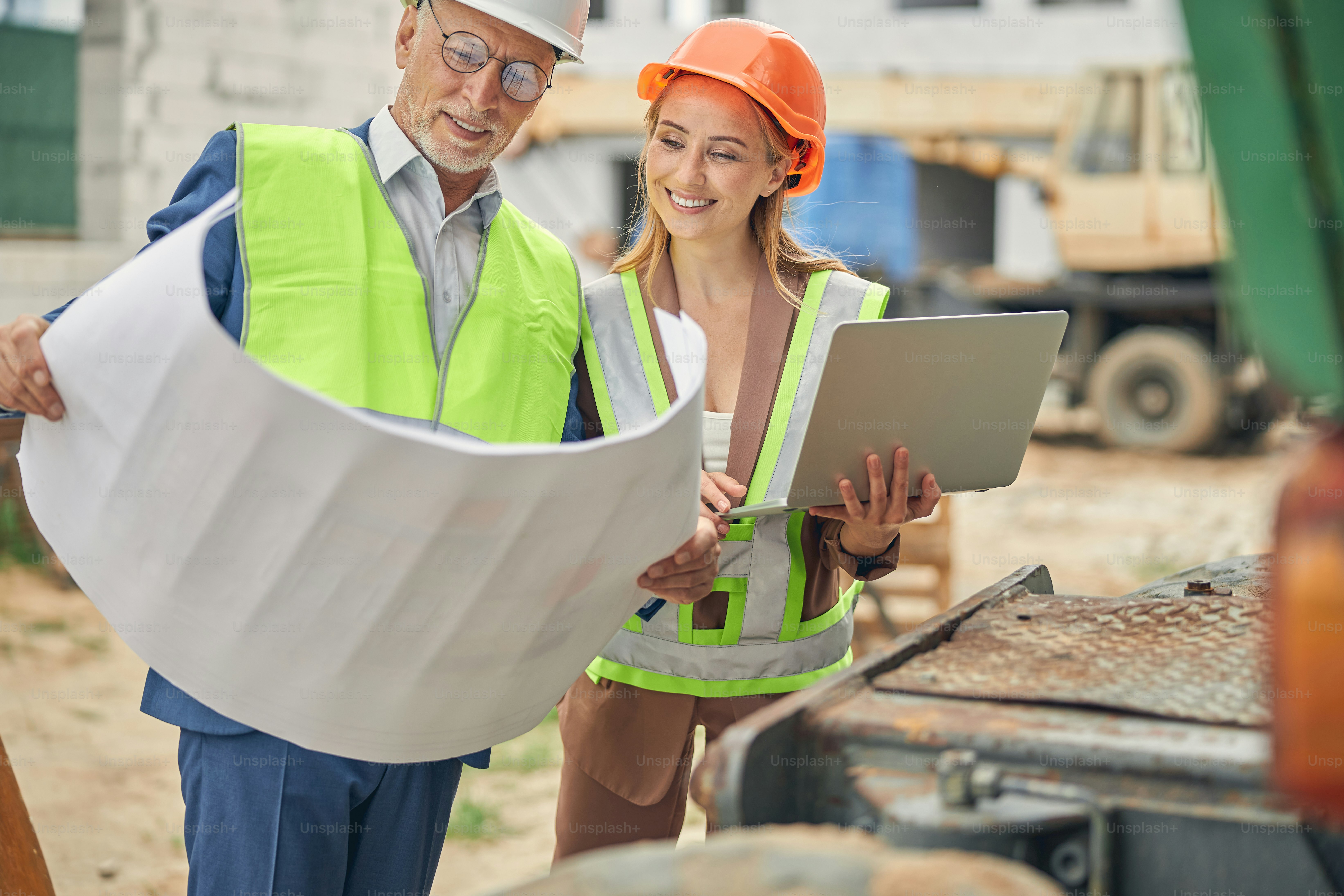 Focused senior man and a smiling female worker with a laptop analyzing a technical drawing