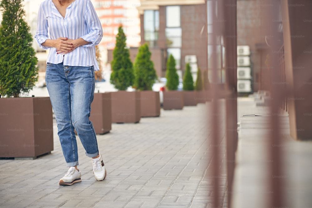 Cropped photo of a slim woman walking down the street with her hands on the stomach
