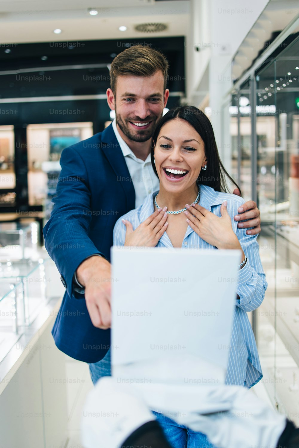 Beautiful couple enjoying in shopping at modern jewelry store. Young woman try it out gorgeous necklace and earrings.