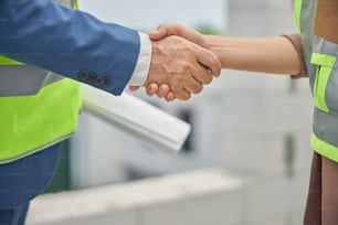 Cropped photo of a Caucasian business lady and an engineer with a drawing greeting each other