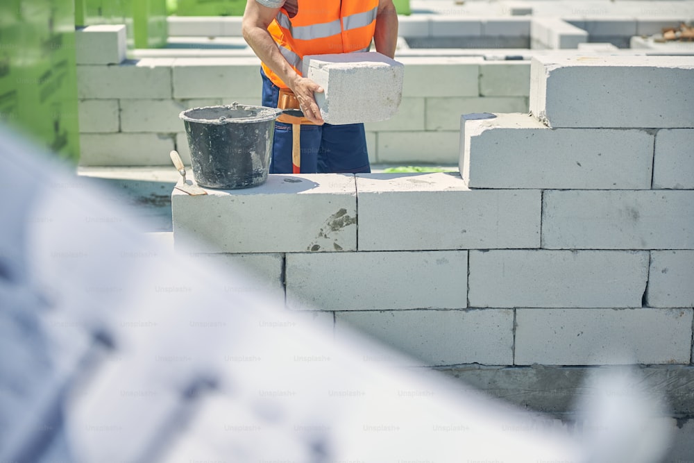 Cropped photo of a fit Caucasian male worker holding a white brick in his hands