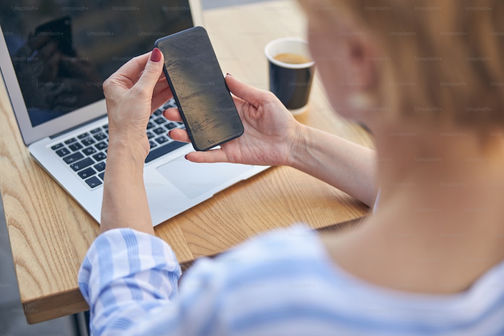 Back view of a lady with a short haircut holding her cellphone with both hands