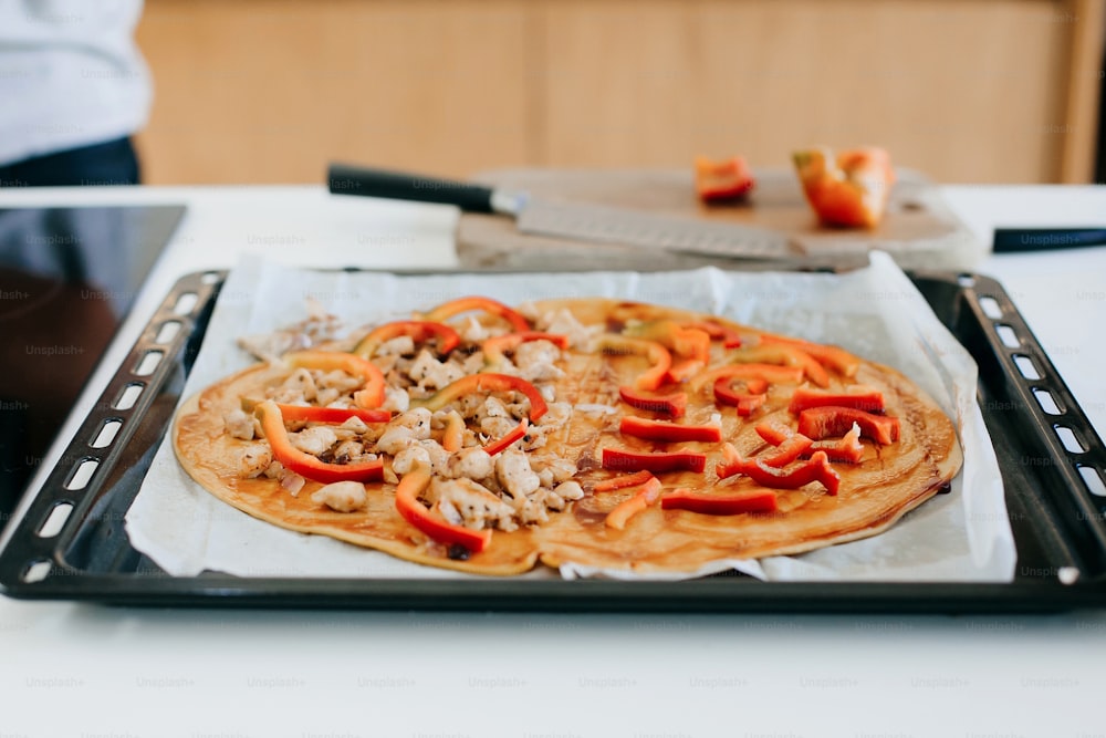 Gebratenes Hähnchen und Pfeffer auf rundem Teig mit Ketchup für Pizza in moderner weißer Küche. Prozess der Herstellung von Heimpizza, Zutaten aus nächster Nähe. Hausmannskost-Konzept