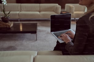 Cropped photo of a lady sitting on a couch, working on her laptop enjoying an empty well-furnished lounge