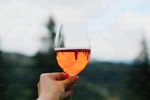 Aperol trinken in der Hand vor dem Hintergrund von Bergen, Sommerurlaub und Resort. Frau jubelt mit leckerem Orangencocktail und feiert im Freien