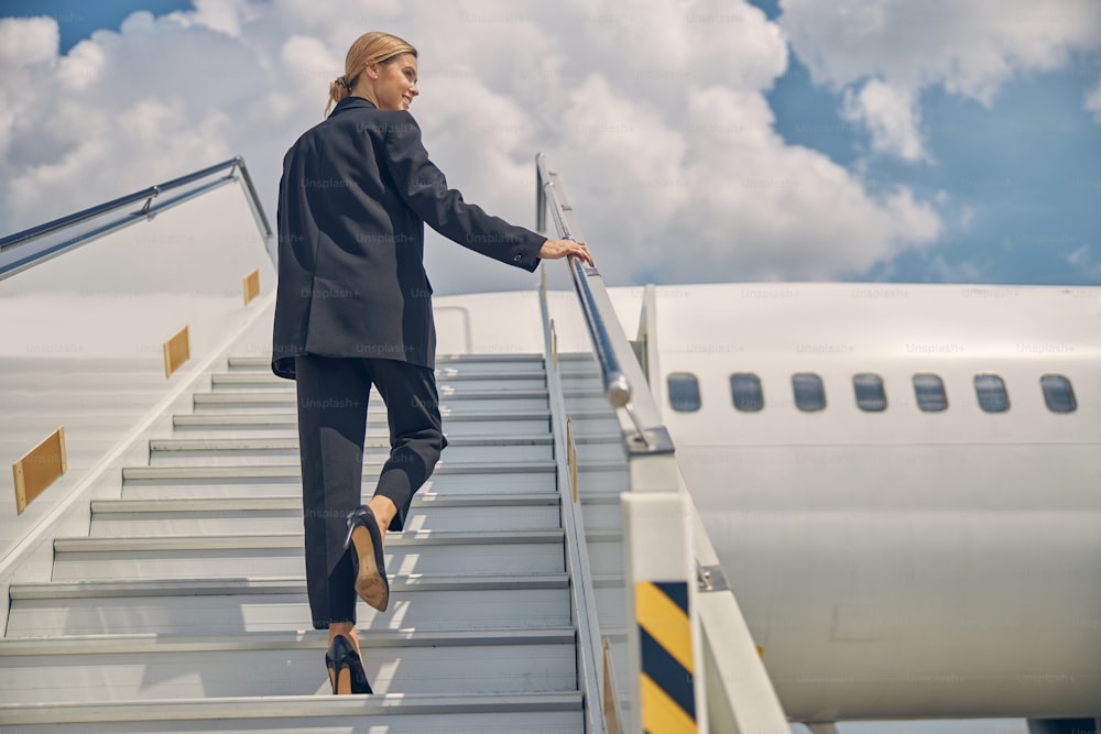 승객 탑승 계단을 오르는 기뻐하는 젊은 백인 공항 여성 직원의 뒷모습