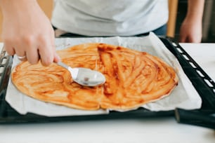 ピザ用のケチャップで丸い生地。モダンな白いキッチンで生生地にトマトソースを塗る人。ホームピザを作るプロセス、材料をクローズアップします。家庭料理のコンセプト