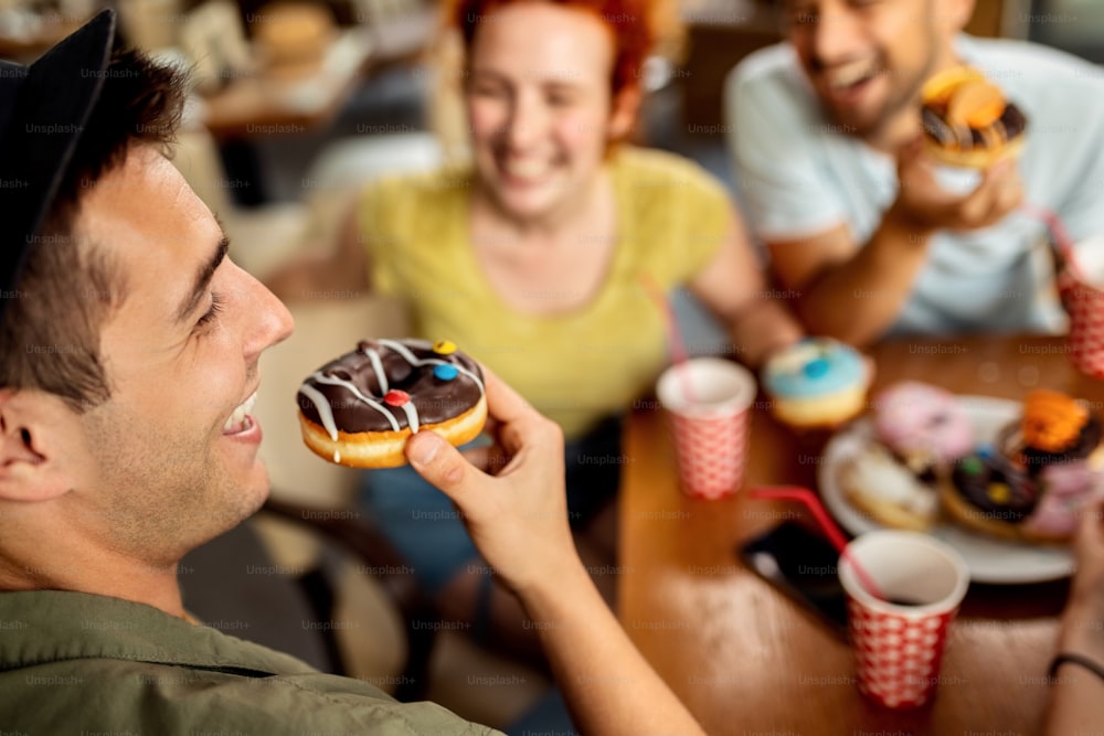 Junger Mann hat Spaß beim Donut-Essen und beim Gespräch mit seinen Freunden in einem Café.