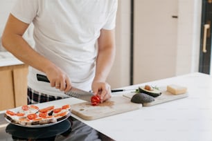 Home cooking concept. Person cutting tomato slice for sandwich on modern white kitchen. Process of making healthy toasts with avocado, tomato, arugula, cheese and whole grain bread.