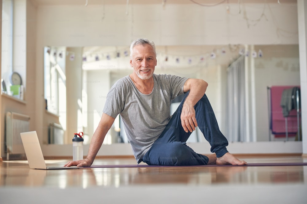 Vista frontal de um homem bonito em forma no tapete de ioga posando para a câmera