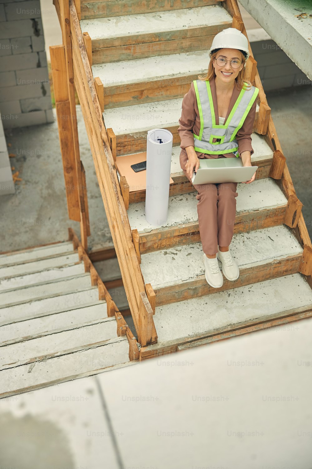 Vista superior de una joven caucásica sonriente con anteojos sentada en las escaleras de concreto