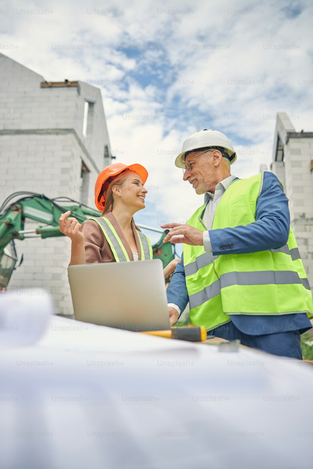 Low angle of a cheerful beautiful Caucasian female worker listening to a senior construction manager