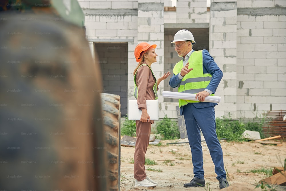 Side view of a female worker communicating with a civil engineer at a building site