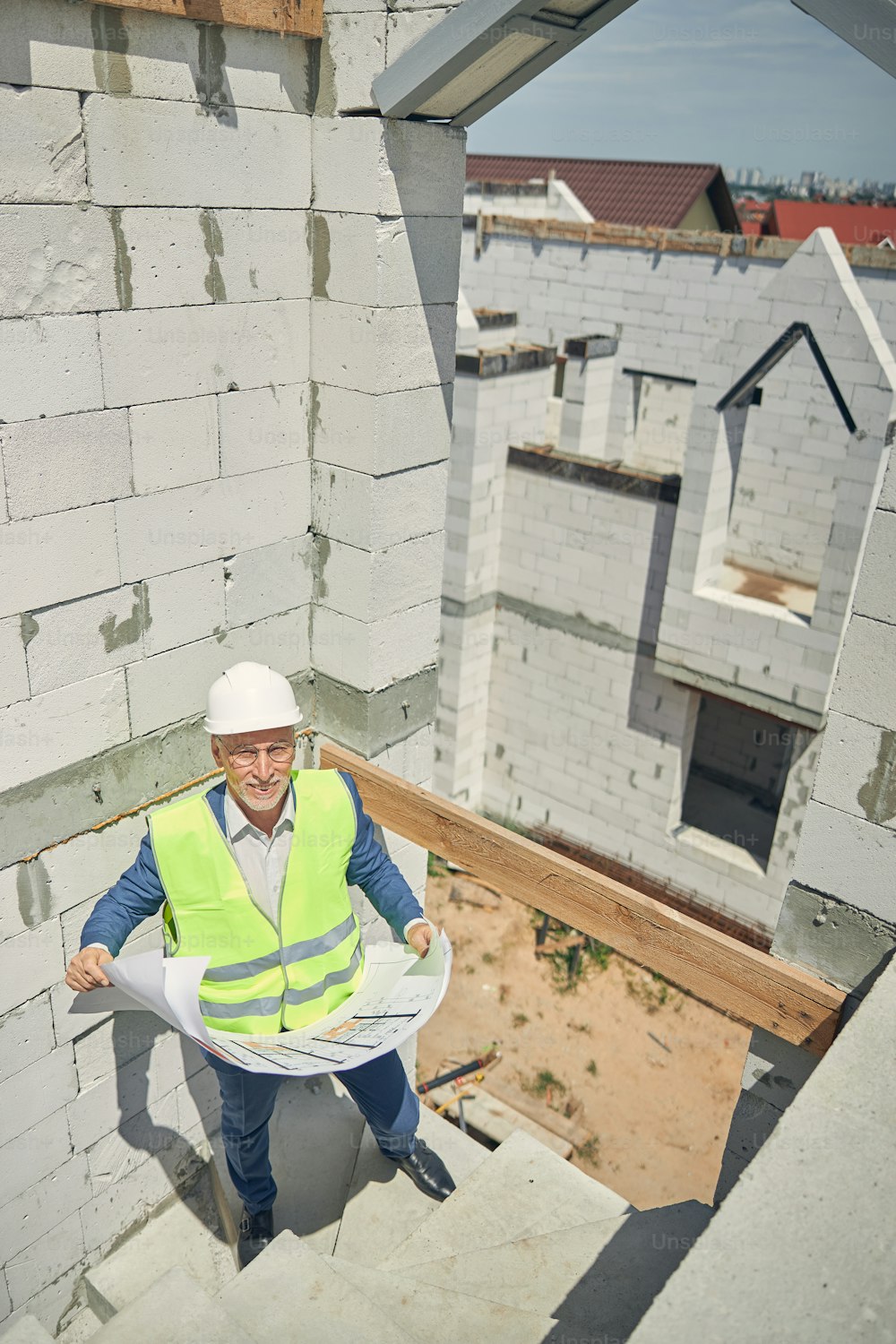 Top view of a smiling civil engineer in a protective helmet with blueprints looking upwards