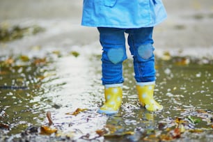 Bambino che indossa stivali da pioggia gialli e salta in una pozzanghera in una giornata autunnale. Bambina che si diverte con l'acqua e il fango nel parco in un giorno di pioggia. Attività autunnali all'aperto per bambini