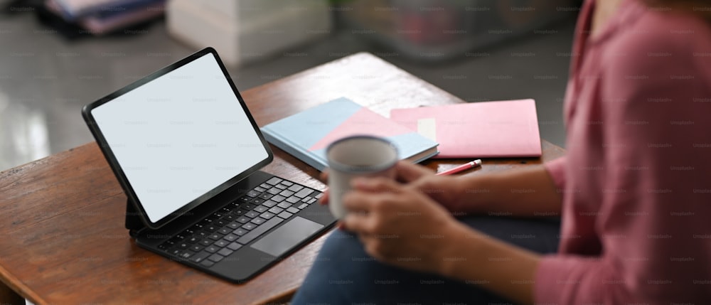 Uma imagem recortada de uma mulher está usando um tablet de computador de tela branca em branco na mesa de madeira.