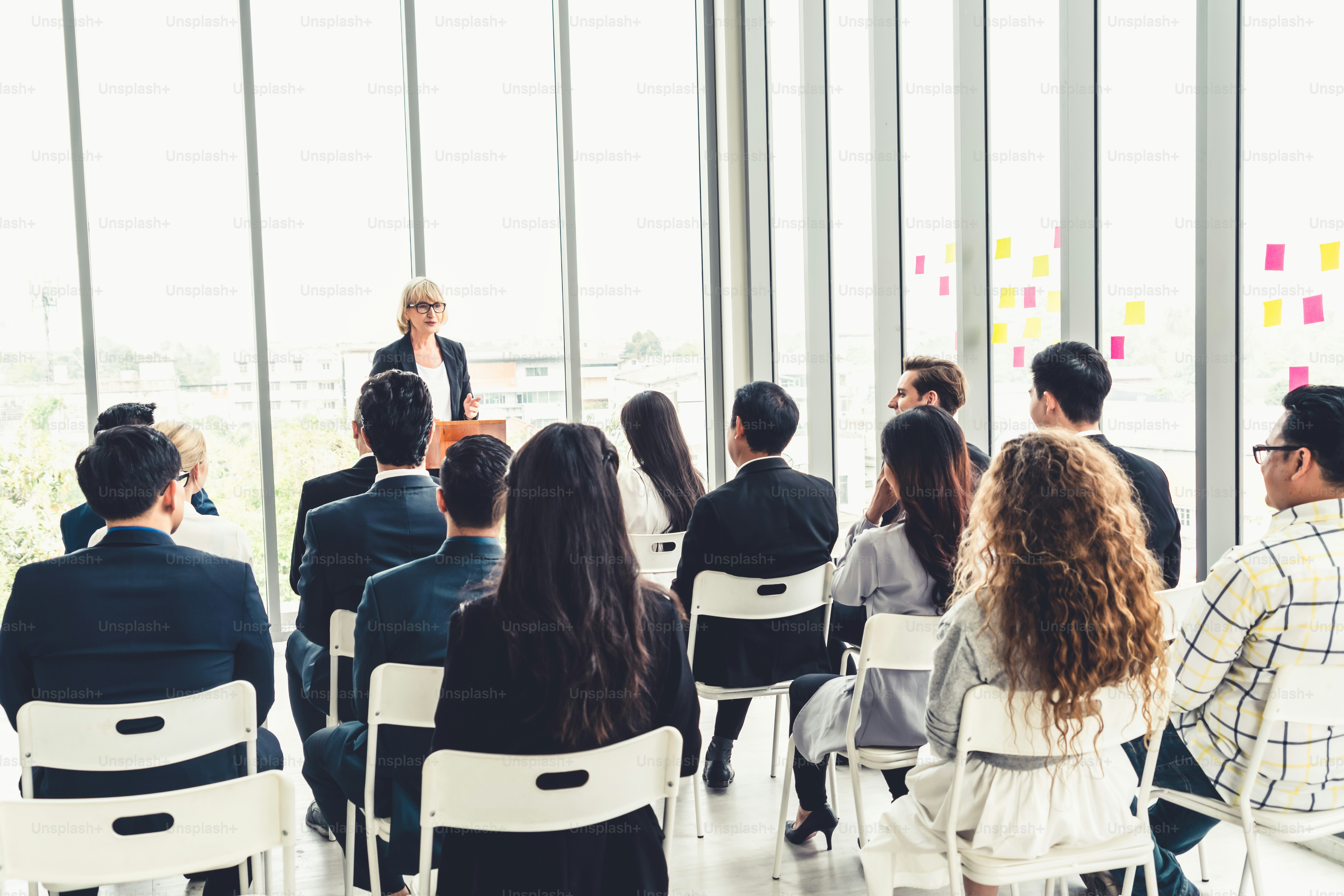 Group of business people meeting in a seminar conference . Audience listening to instructor in employee education training session . Office worker community summit forum with expert speaker .