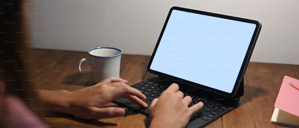 Cropped image of a woman's hands is using a computer tablet at the wooden working desk.