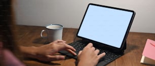 Cropped image of a woman's hands is using a computer tablet at the wooden working desk.
