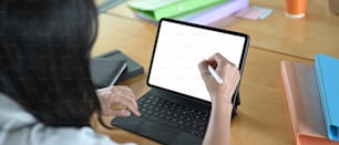 La mujer está usando una tableta de computadora y un lápiz óptico en la mesa de trabajo de madera.
