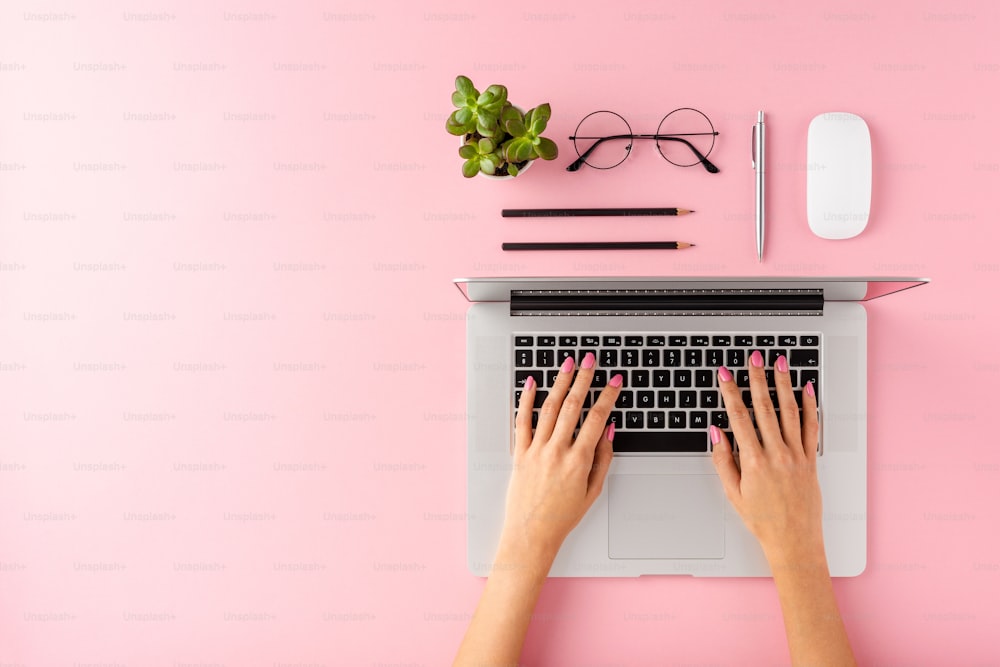 액세서리가 있는 분홍색 배경에 현대 노트북에서 작업하는 여성 손. 사무실 데스크톱. 플랫 레이