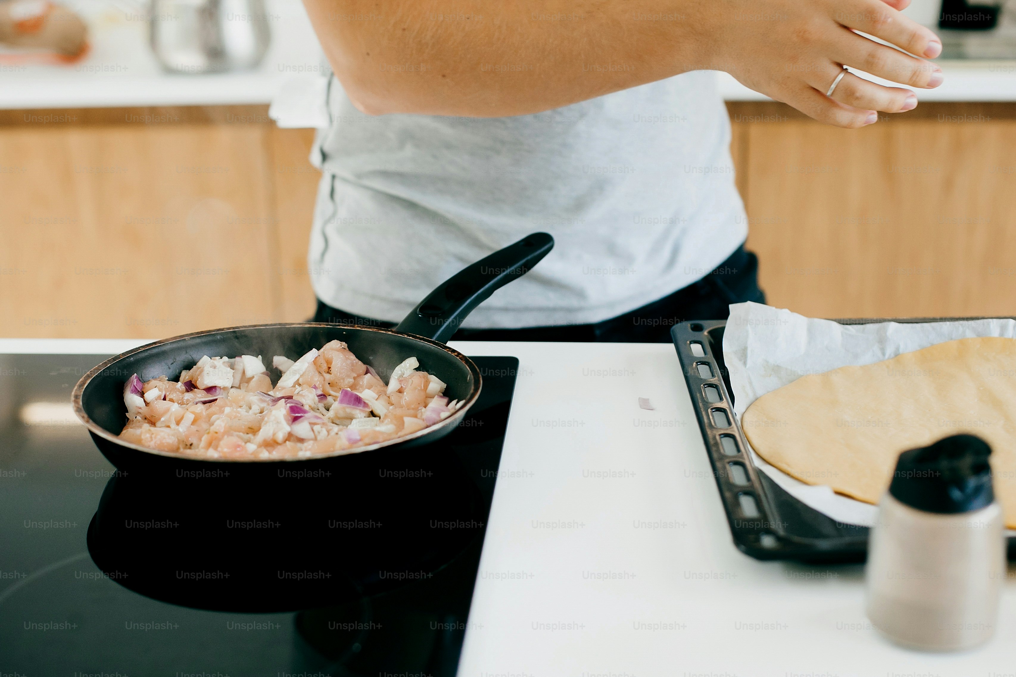 Persona asando cebolla y filete de pollo en estufa eléctrica en cocina blanca moderna. Proceso de elaboración de la pizza casera, los ingredientes se cierran. Concepto de cocina casera