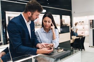Beautiful couple enjoying in shopping at modern jewelry store while trying out and buying watches.
