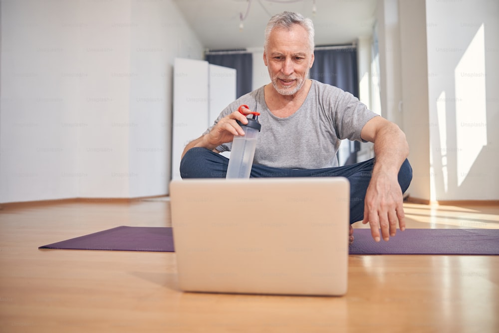 Vista frontal de un hombre concentrado sentado con las piernas cruzadas en la colchoneta de ejercicios en un estudio de fitness