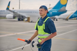 Calm aircraft marshaller with wands and a headset in his hands standing at the airdrome
