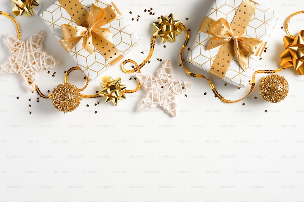 Weihnachtskarte mit Geschenken, luxuriösen goldenen Dekorationen, Bällen, Konfetti auf weißem Hintergrund. Flache Lage, Draufsicht. Weihnachtsrahmen, Neujahrsbanner-Mockup