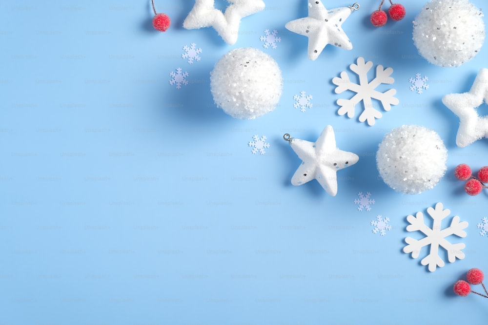 Blue Christmas background with white decorations, balls, stars, snowflakes, red berries. Flat lay, top view, copy space. Xmas greeting card template, seasonal holiday banner mockup