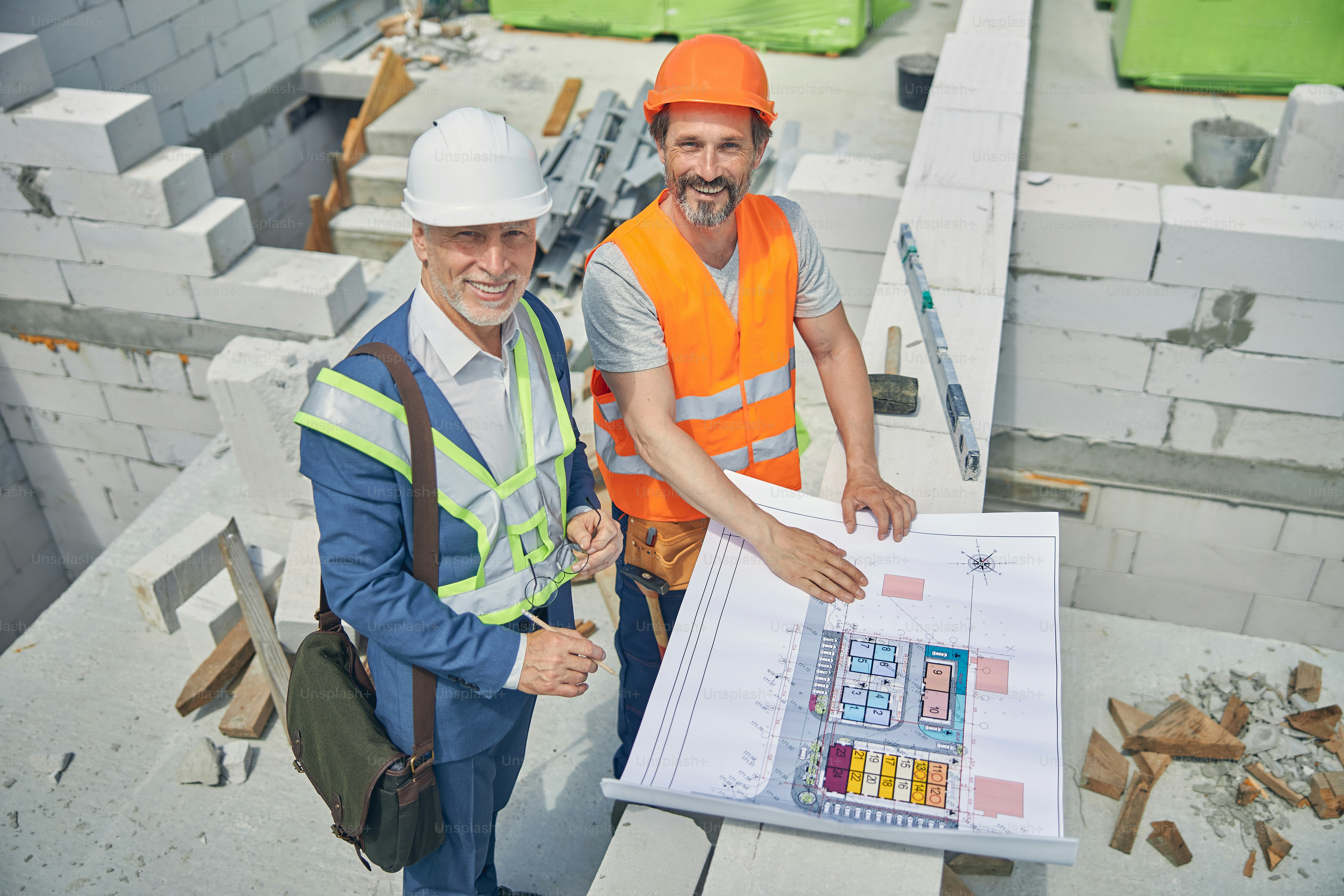 Top view of two smiling adult Caucasian men in safety helmets posing for the camera