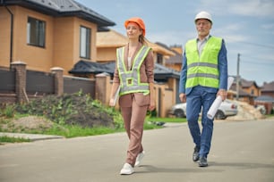 Full-length portrait of a serene woman and a serious civil engineer walking along the street