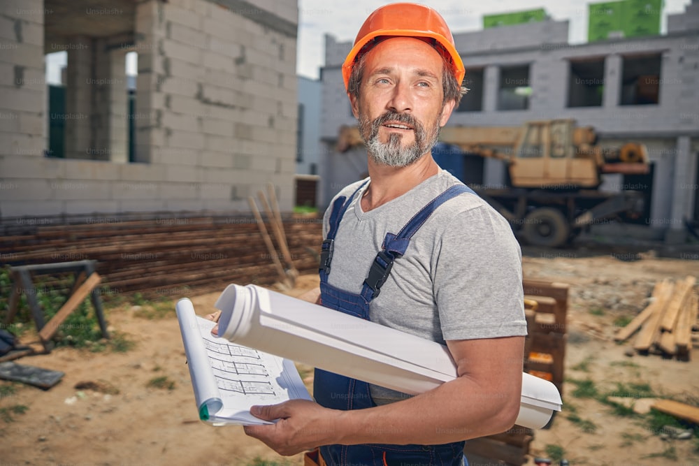 Handsome male worker with a roll of paper under his arm gazing into the distance