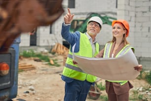 Vue de face d’une dame souriante avec un plan de maison debout à côté d’un constructeur