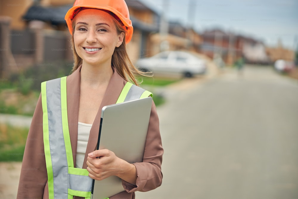 Waist-up portrait of a smiling Caucasian female engineer standing in the middle of the street