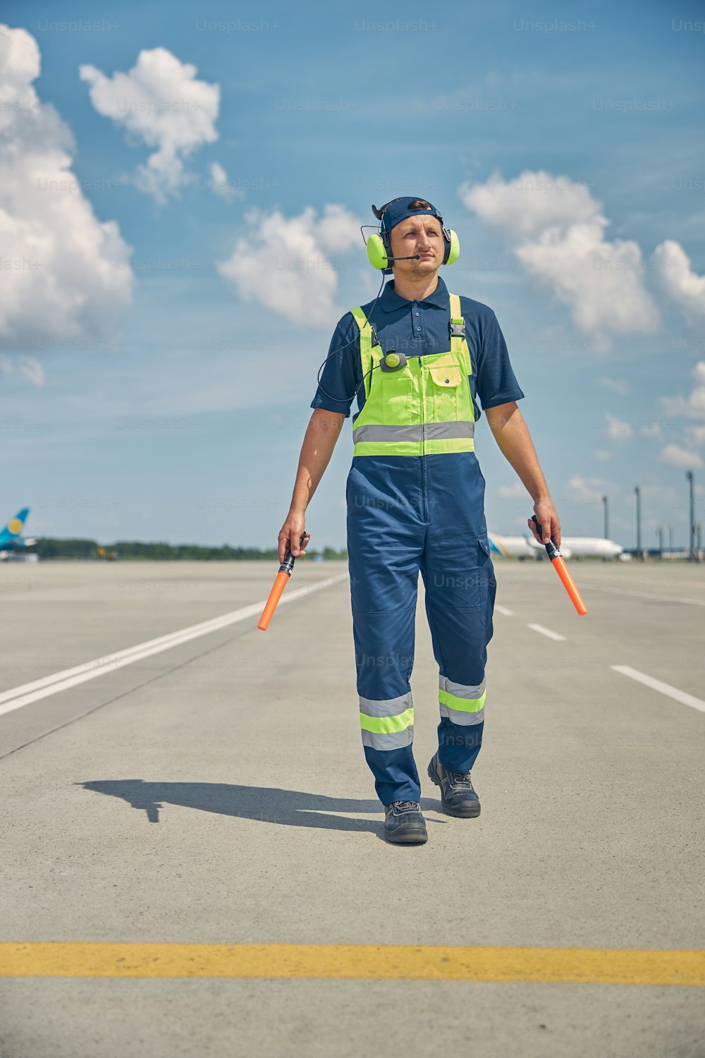 Full-length portrait of an aircraft marshaller with a pair of wands staring into the distance